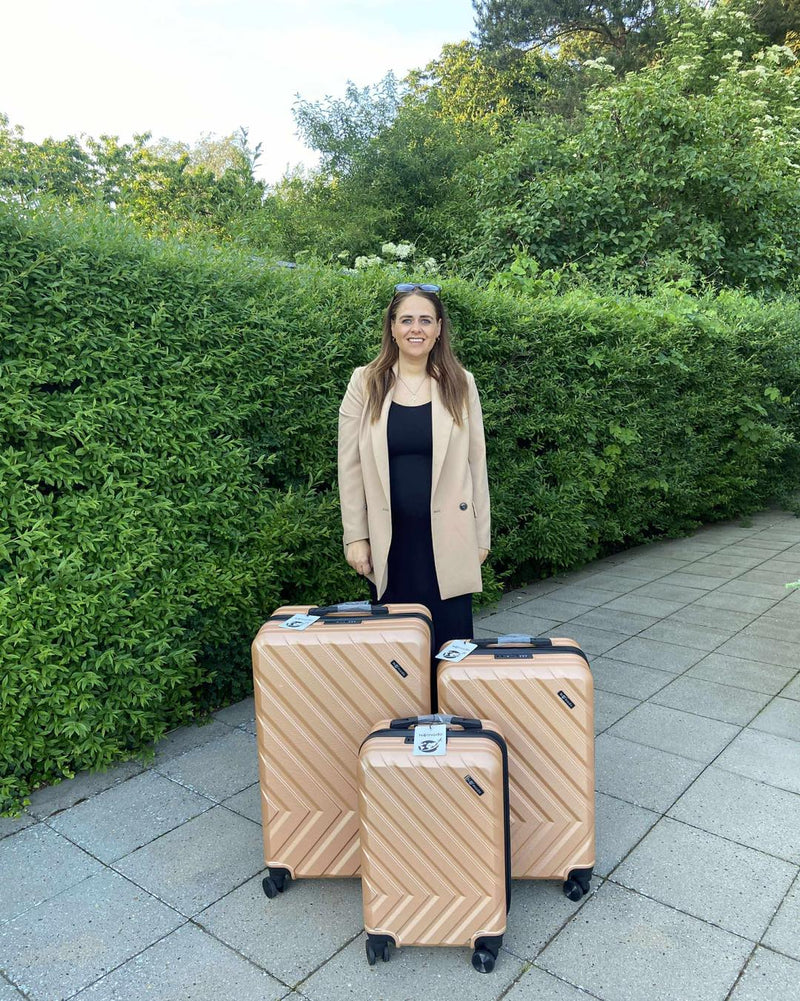 Woman with three champagne-coloured Nomado Horizon suitcases outdoors by a hedge